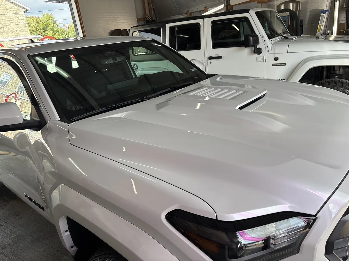 Glossy white Toyota Tacoma hood and headlight in the shop