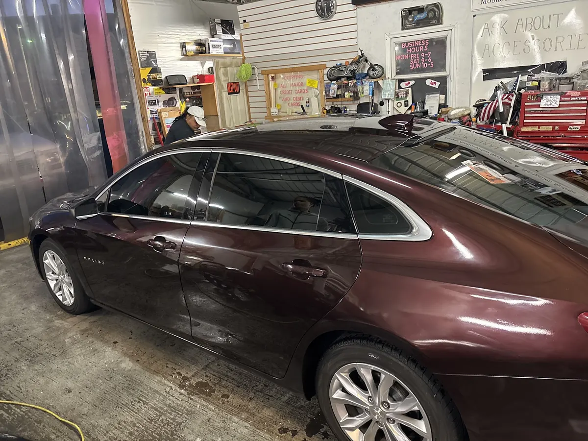 Maroon Chevrolet Malibu with tinted windows inside the shop, accessories wall behind